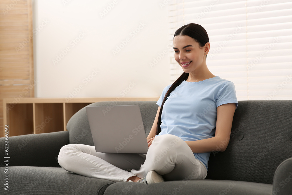 Naklejka premium Happy woman working with laptop on sofa at home