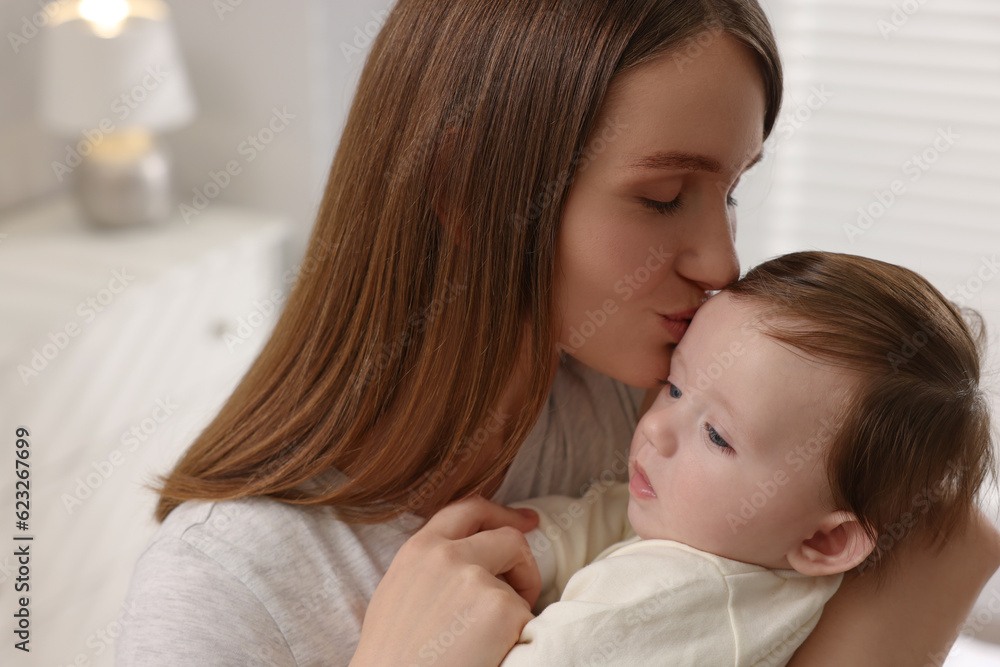 Happy mother kissing her little baby indoors, closeup Happy mother kissing her little baby indoors, closeup