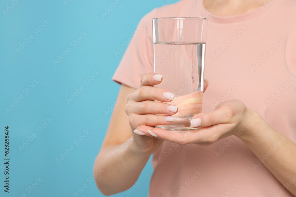 Healthy habit. Closeup of woman holding glass with fresh water on light blue background, space for text Healthy habit. Closeup of woman holding glass with fresh water on light blue background, space for text
