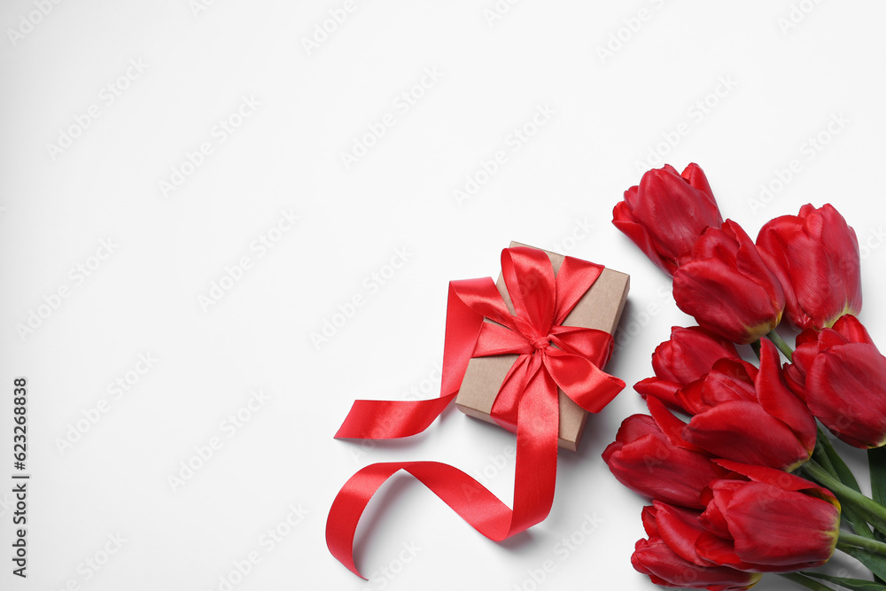 Beautiful gift box and red tulip flowers on white background, flat lay. Space for text Beautiful gift box and red tulip flowers on white background, flat lay. Space for text