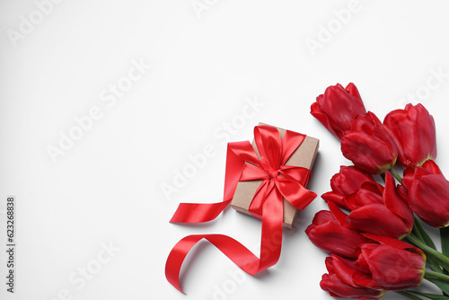 Beautiful gift box and red tulip flowers on white background, flat lay. Space for text