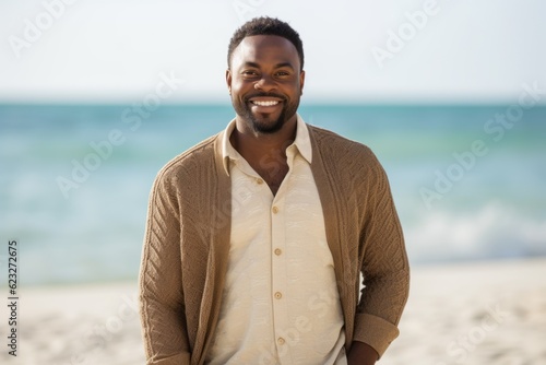 Portrait of smiling young man standing on beach with hands in pockets