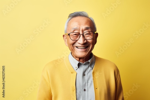 Portrait of happy asian senior man in yellow sweater on yellow background