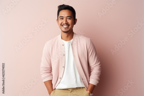 Handsome young Asian man smiling and looking at camera while standing against pink background © Leon Waltz