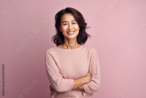 Smiling asian woman with crossed arms looking at camera over pink background