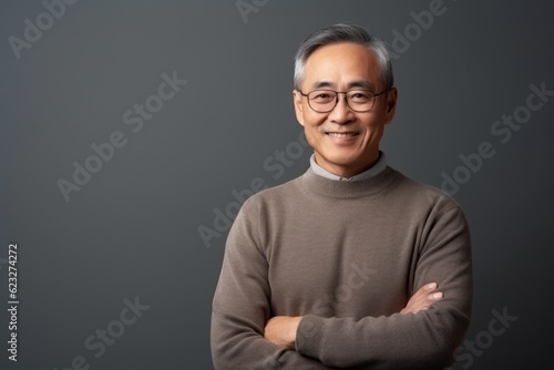 Portrait of an asian senior man with arms crossed against grey background © Anne Schaum