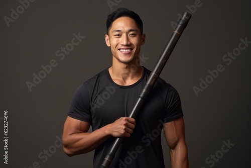 Portrait of a young asian man holding baseball bat on grey background