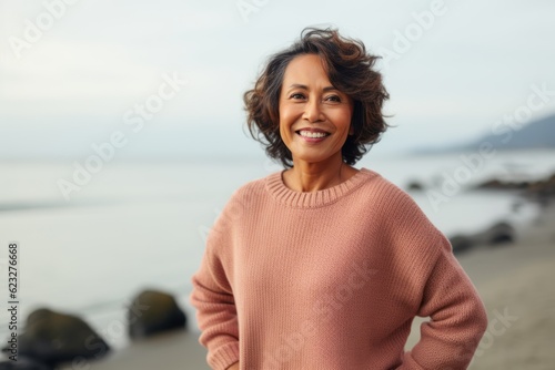 Portrait of smiling mature woman standing on beach with hands on hips © Anne Schaum