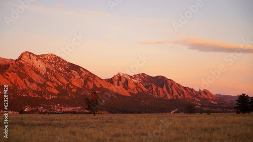 Stunning deep orange pink sunrise sunset Colorado University Boulder Flat irons late fall winter dead yellow grass snow on red rocks peaks early morning pan to the left slow motion photo