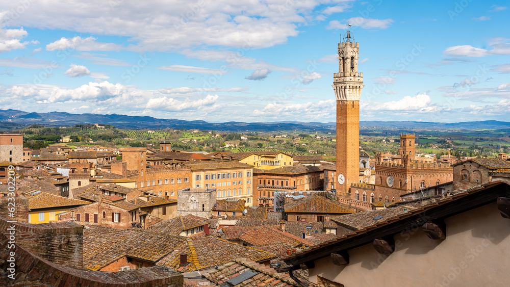 Daytime  cityscape view of the Tuscan town of Siena, Italy. View as seen from the top of the Duomo di Siena cathedral, with the Torre del Mangia tower prominent on the right side of the frame.

