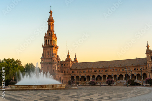 Daytime landscape image of the Plaza de Espana in Seville, Spain.  Part of the building is lit with golden sunrise light, and a fountain is flowing in front of the building.