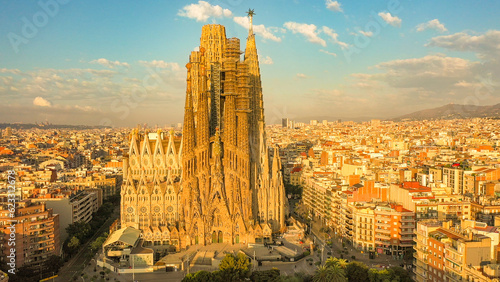 Aerial sunrise image of the Sagrada Familia cathedral in Barcelona, Spain. The cathedral is bathed in golden light, set against the Barcelona cityscape. 