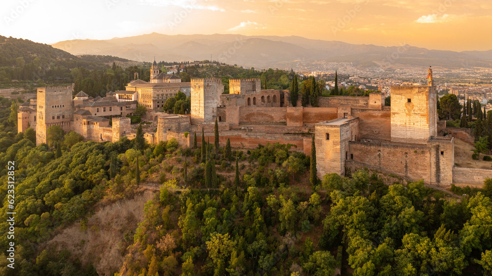 The Alhambra fortress in Granada, Spain at sunrise. Fortress is bathed in golden-reddish light.