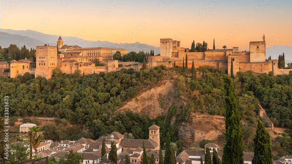 The Alhambra fortress in Granada, Spain during sunset. Fortress is bathed in golden-reddish light.