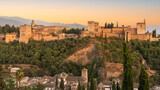 The Alhambra fortress in Granada, Spain during sunset. Fortress is bathed in golden-reddish light.