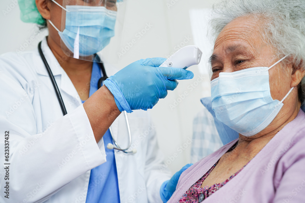 Doctor in ppe user infrared thermometer to check temperature of asian elderly woman patient for safety to protect covid 19 virus. Doctor in ppe user infrared thermometer to check temperature of asian elderly woman patient for safety to protect covid 19 virus.