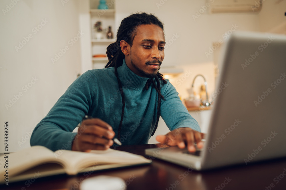 A focused Arabic man is sitting at home with his agenda and finishing tasks on a laptop. A focused Arabic man is sitting at home with his agenda and finishing tasks on a laptop.