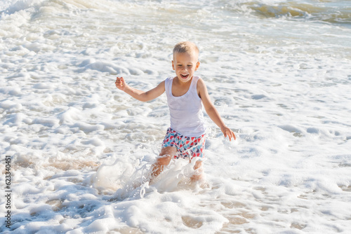 a little boy runs joyfully along the seashore on a sunny summer day, a happy child
