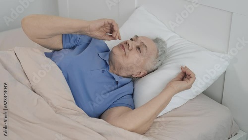 A senior citizen woman can't sleep in bed, tormented by insomnia. An old woman is troubled by thoughts before going to bed.