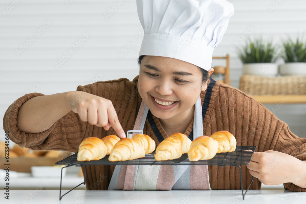 Closeup of smiling woman in apron and chef hat baking pastry at home, looking and checking delicious baked croissants out of oven. Joyful homemade baker with bread at cozy kitchen Closeup of smiling woman in apron and chef hat baking pastry at home, looking and checking delicious baked croissants out of oven. Joyful homemade baker with bread at cozy kitchen