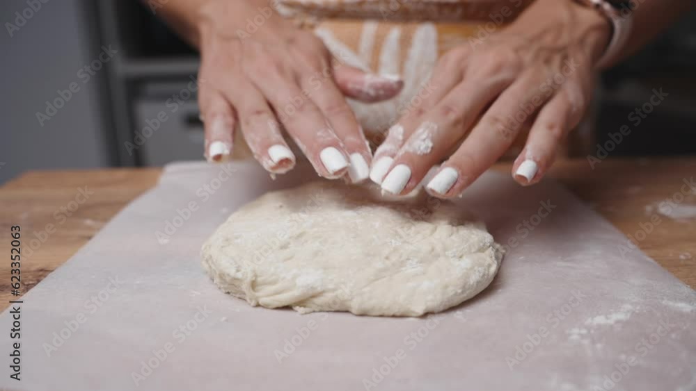 A young woman sprinkles flour on a lump of dough on the table, and the scene is captured in slow motion. A young woman sprinkles flour on a lump of dough on the table, and the scene is captured in slow motion.