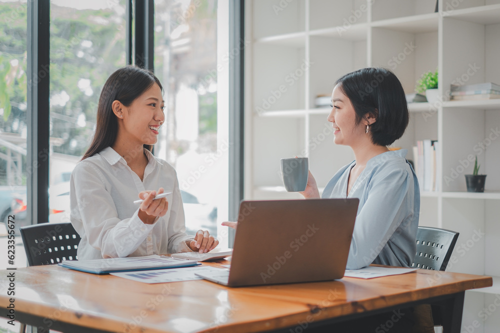 Two women analyzing documents while sitting on a table in office. Woman executives at work in office discussing some paperwork. Two women analyzing documents while sitting on a table in office. Woman executives at work in office discussing some paperwork.