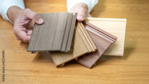 Designer hand choosing wood texture laminate material samples for wall and floor skirting design. Wooden piece catalog guide for interior architecture detail work.