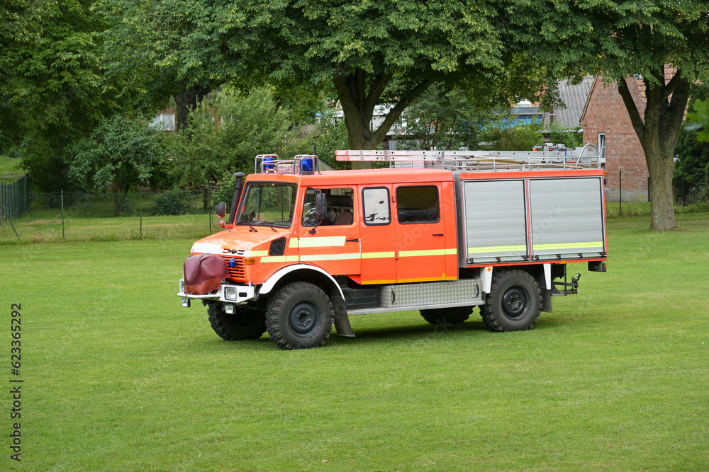 German fire engine, red orange truck with ladders on the roof and equipment for firefighting operations behind roller shutter doors on a meadow, copy space German fire engine, red orange truck with ladders on the roof and equipment for firefighting operations behind roller shutter doors on a meadow, copy space