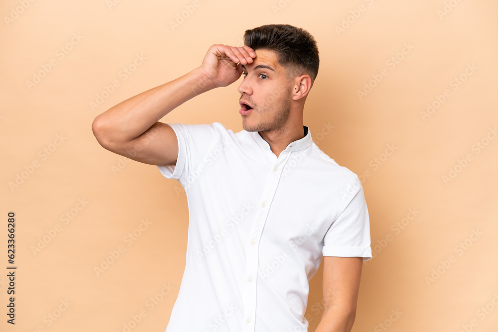 Young caucasian man isolated on beige background doing surprise gesture while looking to the side Young caucasian man isolated on beige background doing surprise gesture while looking to the side