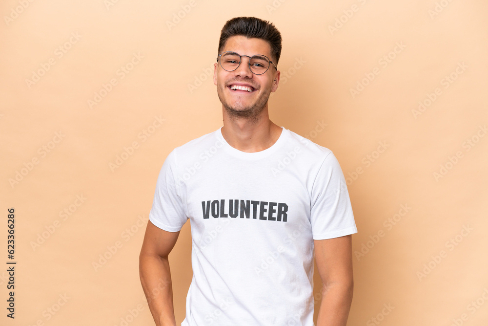 Young volunteer caucasian man isolated on beige background laughing Young volunteer caucasian man isolated on beige background laughing
