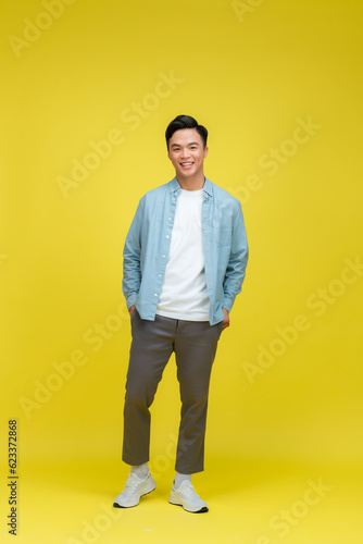 Full length portrait of asian young smiling man standing on yellow background