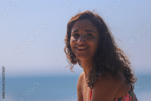 Linda e jovem mulher brasileira posa numa praia para paradisíaca com seu biquini colorido e sorriso radiante