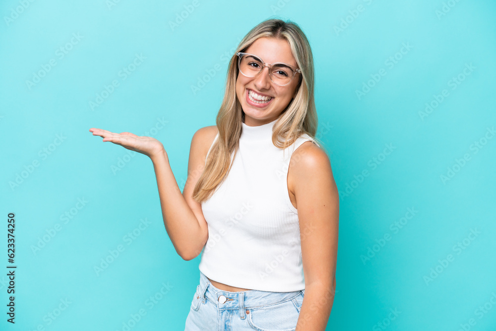 Fototapeta premium Young caucasian woman isolated on blue background holding copyspace imaginary on the palm to insert an ad