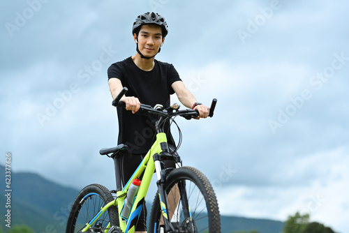 Portrait of young man with bicycle standing in the park with beautiful mountains on background
