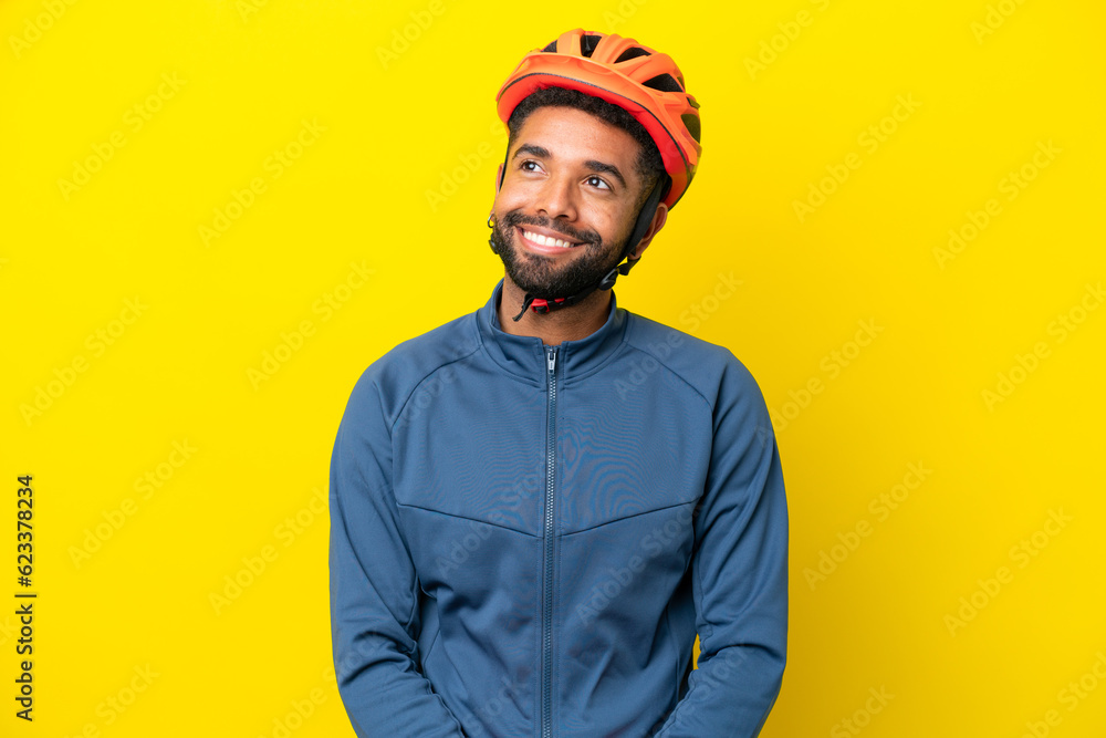Young cyclist Brazilian man isolated on yellow background thinking an idea while looking up