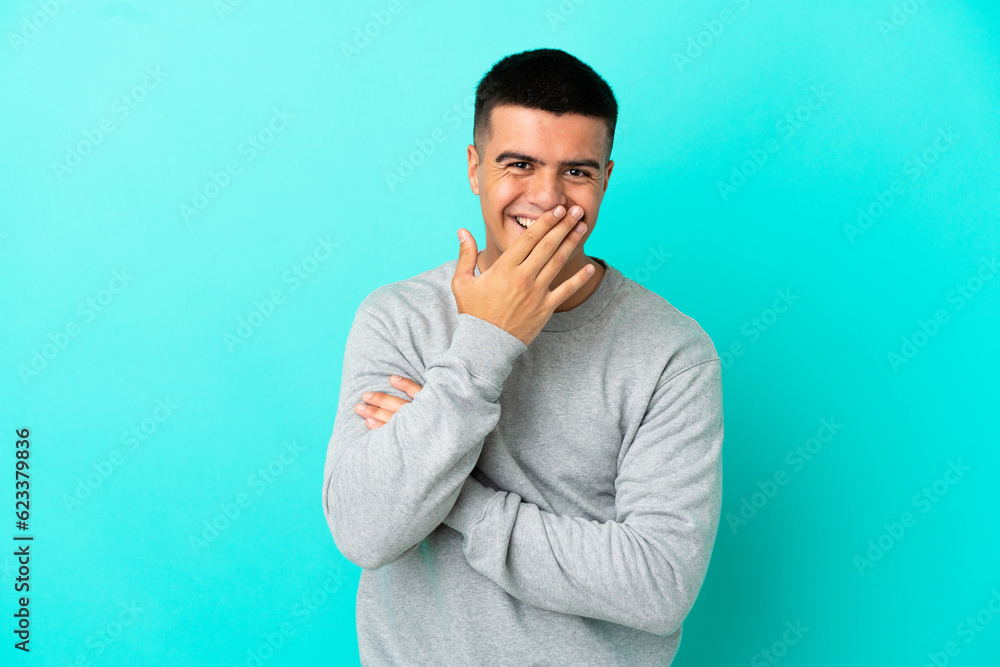 Young handsome man over isolated blue background happy and smiling covering mouth with hand Young handsome man over isolated blue background happy and smiling covering mouth with hand