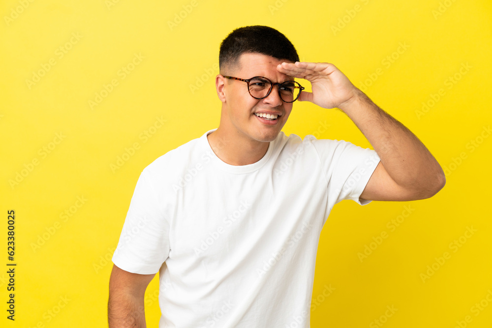 Young handsome man over isolated yellow background looking far away with hand to look something Young handsome man over isolated yellow background looking far away with hand to look something