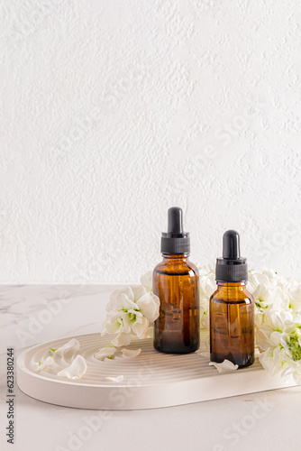 Brown amber bottles with anti-aging facial skin care product on a white plaster tray with white flowers. rejuvenating effect. Vertical view.