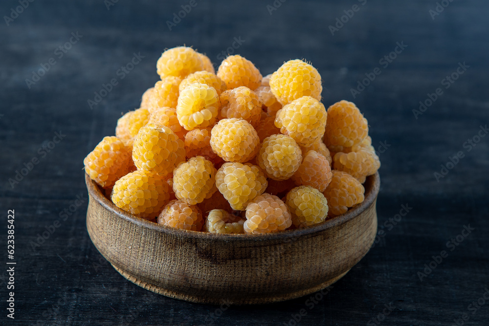 Yellow raspberries in a wooden bowl on the table. Summer berries background. Vitamin food, berry harvest. Healthy nutrition. Yellow raspberries in a wooden bowl on the table. Summer berries background. Vitamin food, berry harvest. Healthy nutrition.