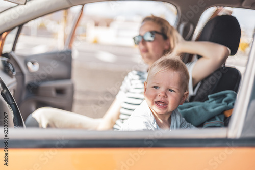 Mother and her infant baby boy child on family summer travel road trip, sitting at dad's front seat, waiting in the car for father to buy farry tickets