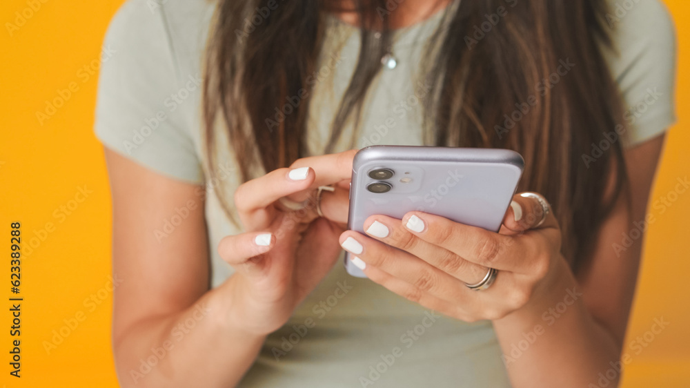 Close-up, hands of unrecognizable girls using phone , isolated over yellow background in studio Close-up, hands of unrecognizable girls using phone , isolated over yellow background in studio