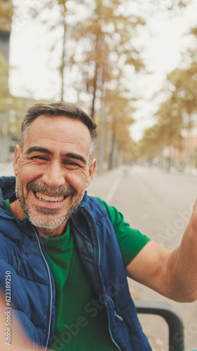 Mature man wearing casual clothes  sitting on bench in the park  talking on video call from smartphone