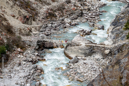 Aerial view of small wooden bridge over dudhkoshi river in nepal. Rocks, pebbles and stones near white water river bank. Barren landscape near pangboche enroute everest base camp trek in nepal. photo