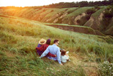 Parents, man and woman going hiking with their children, lying on field and looking at beautiful hills landscape. Warm evening, sunset. Concept of leisure time, fun, nature, active lifestyle