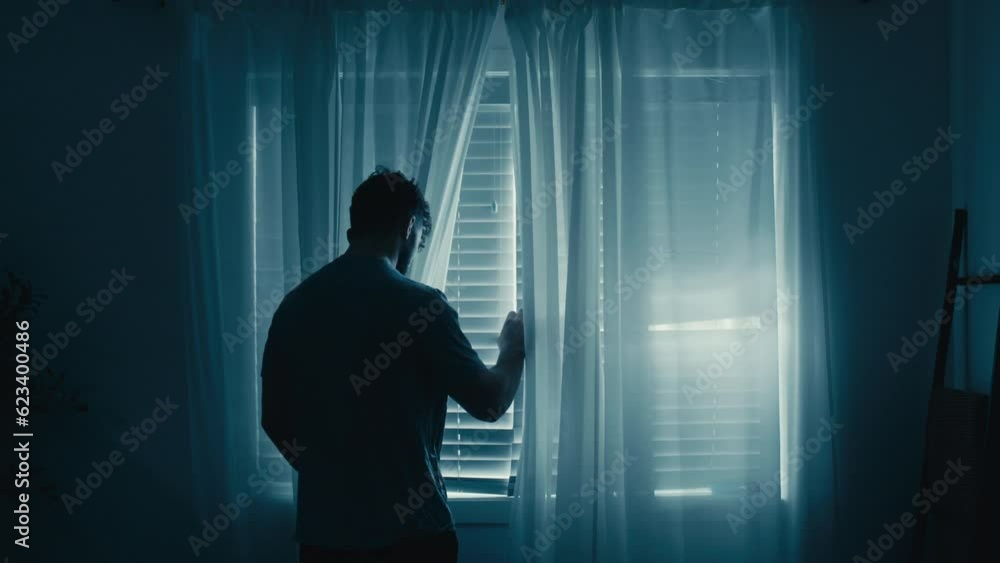 Silhouette of man peering looking through blinds outside, moody blue vibe Silhouette of man peering looking through blinds outside, moody blue vibe