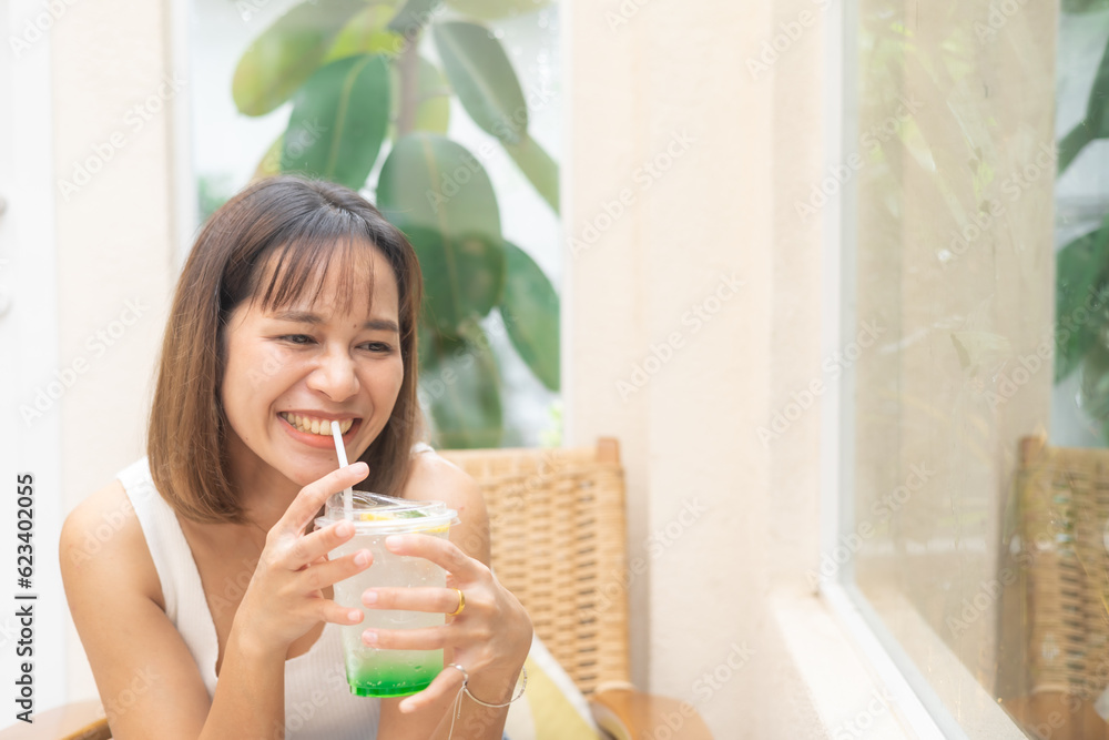 Young Asian woman smiling with apple soda, A woman holding a glass of apple soda with feeling happy and enjoy to eat food in the restaurant. Enjoy eating, refreshing summer drinks, Taste concept. Young Asian woman smiling with apple soda, A woman holding a glass of apple soda with feeling happy and enjoy to eat food in the restaurant. Enjoy eating, refreshing summer drinks, Taste concept.