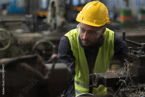 Male engineer worker working with lathe machine in industry factory, wearing safety uniform, helmet. Male technician worker maintenance parts of machine in workshop