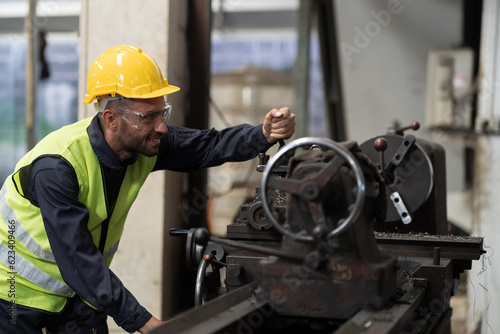 Male engineer worker working with lathe machine in industry factory, wearing safety uniform, helmet. Male technician worker maintenance parts of machine in workshop