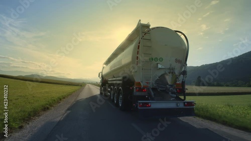 Sunlit oil tanker driving on road at sunset back view tracking shot. Fuel truck riding on countryside highway, transporting liquid on summer