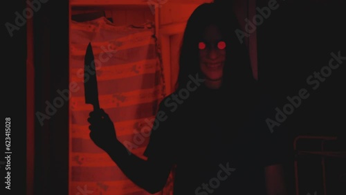 Creepy zombie girl holding a knife and smiling at the camera. Victim POV. Vintage horror video. Handheld shaky camera. Red backlit silhouette. Halloween theme.